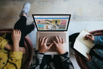 une personne sur son ordinateur et 2 autres personnes qui l'entourent